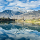 Snow-capped mountains reflected in serene alpine lake with autumn trees under cloudy sky