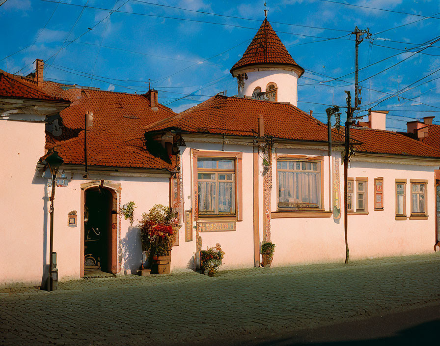 Traditional House with Red-Tiled Roof and Tower Structure on Cobblestone Street