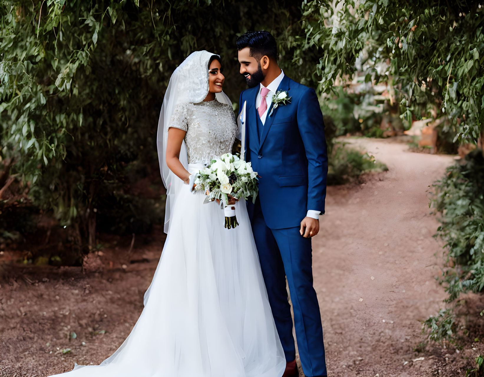 Bride and groom holding hands under leafy archway