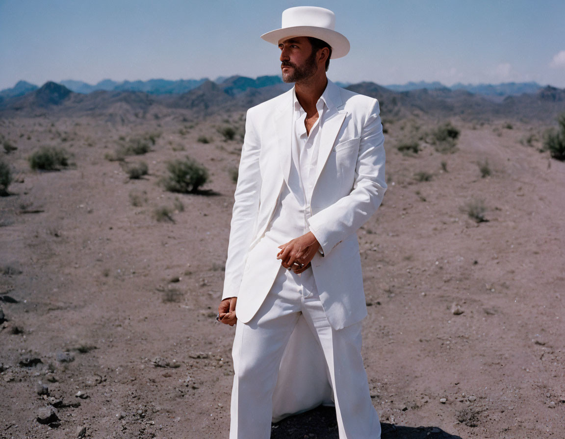 Man in White Suit and Hat Standing in Desert Landscape with Clear Blue Sky