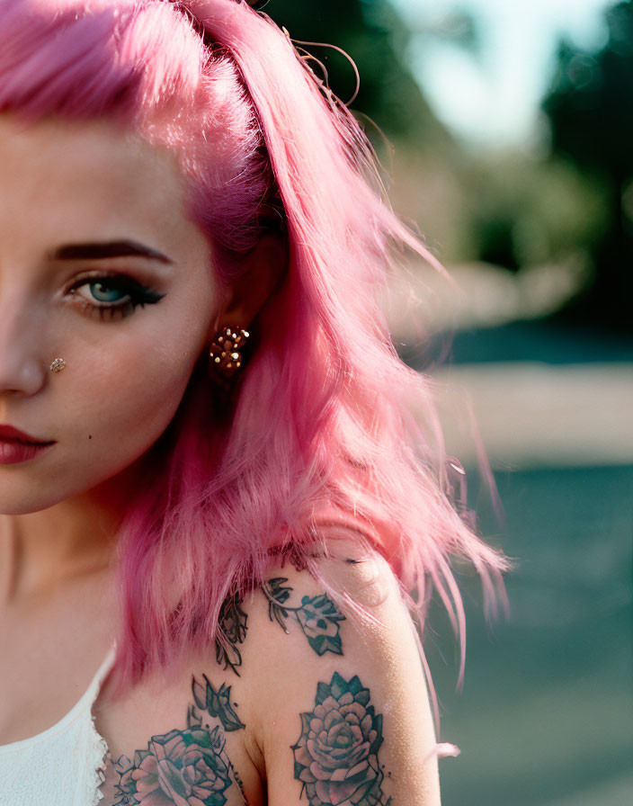 Pink-haired woman with shoulder tattoos gazing at camera in natural setting