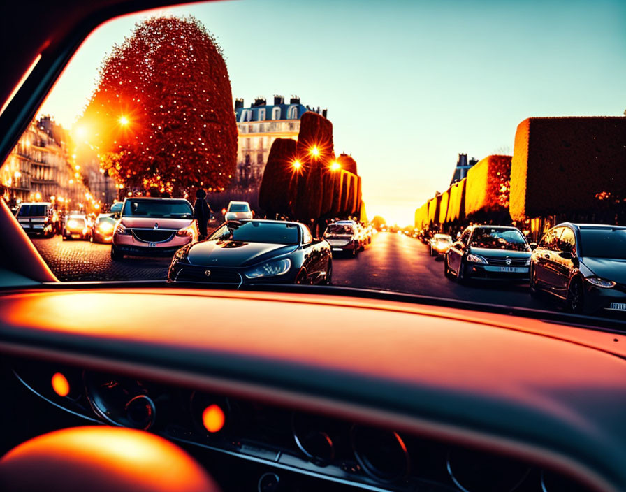 City street at sunset from car interior with lined vehicles and trimmed trees