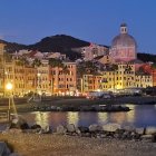 Illuminated classical cityscape at twilight with domed buildings, bridge, and boats.