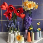 Colorful Artificial Flowers in Stylish Vases on Shelf with Purple Backdrop