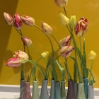 Colorful flowers in blue-gray vases on windowsill against yellow backdrop