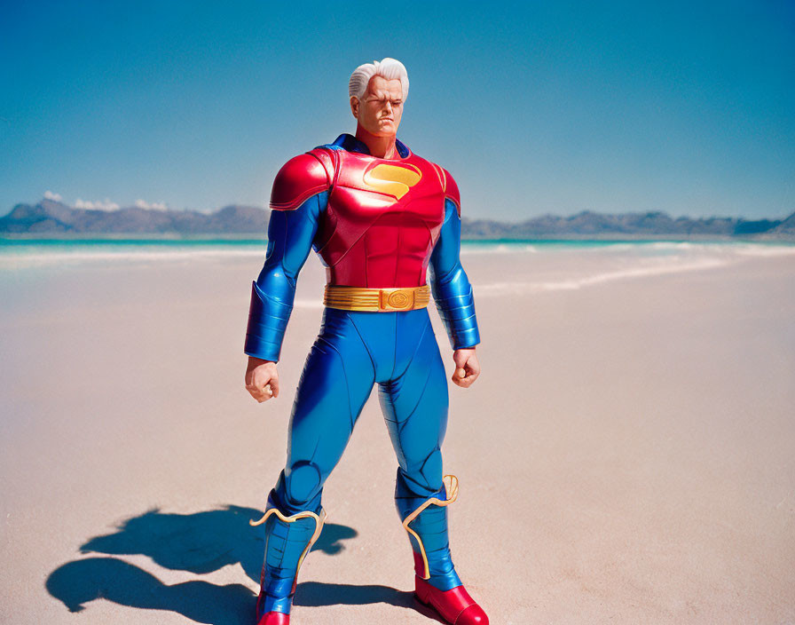 Superhero figurine with red cape and 'S' emblem on sandy beach