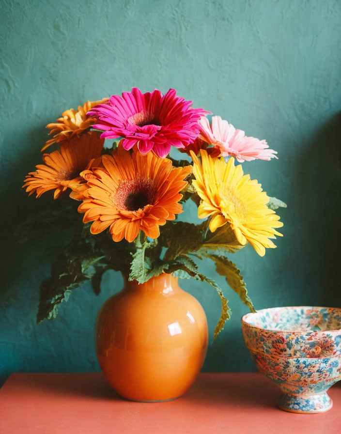 Colorful Gerbera Daisies Bouquet in Orange Vase with Patterned Bowl on Te