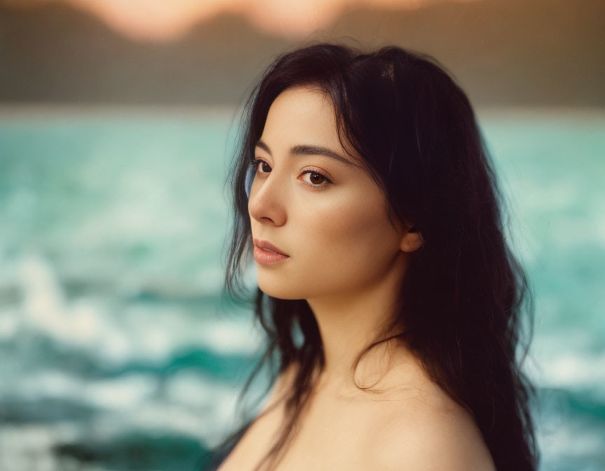 Dark-haired woman portrait against serene ocean twilight.