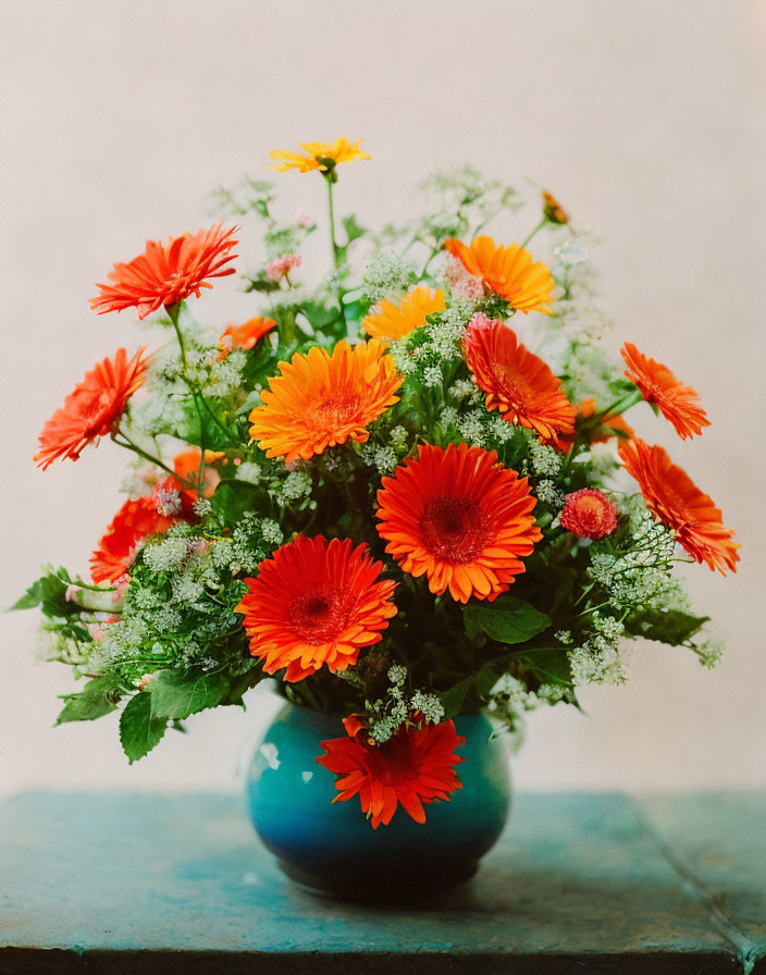 Bright orange and yellow gerbera bouquet in blue vase on rustic table