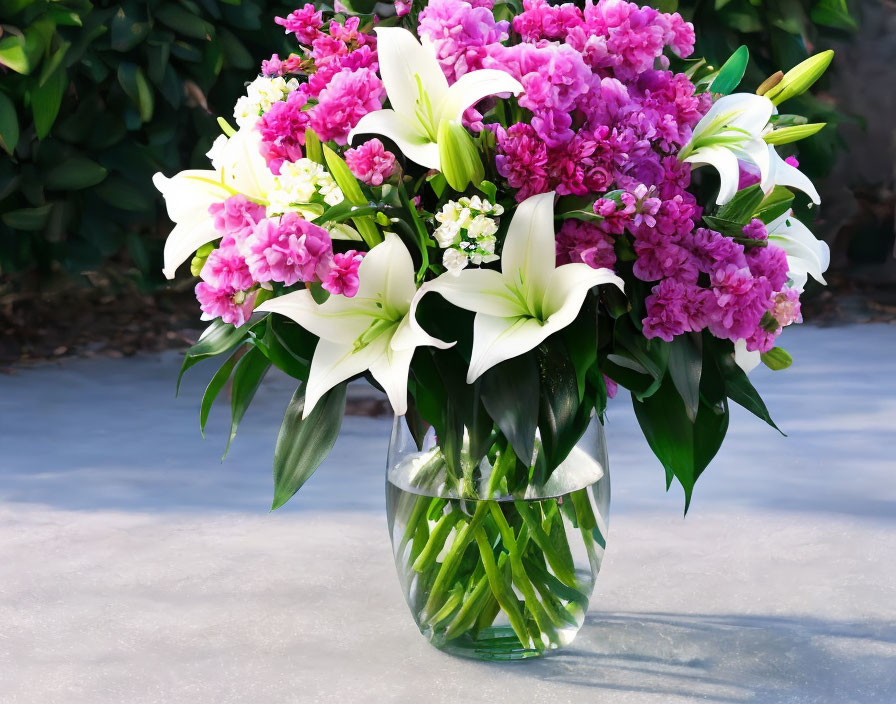 White lilies and pink flowers in clear vase with green foliage