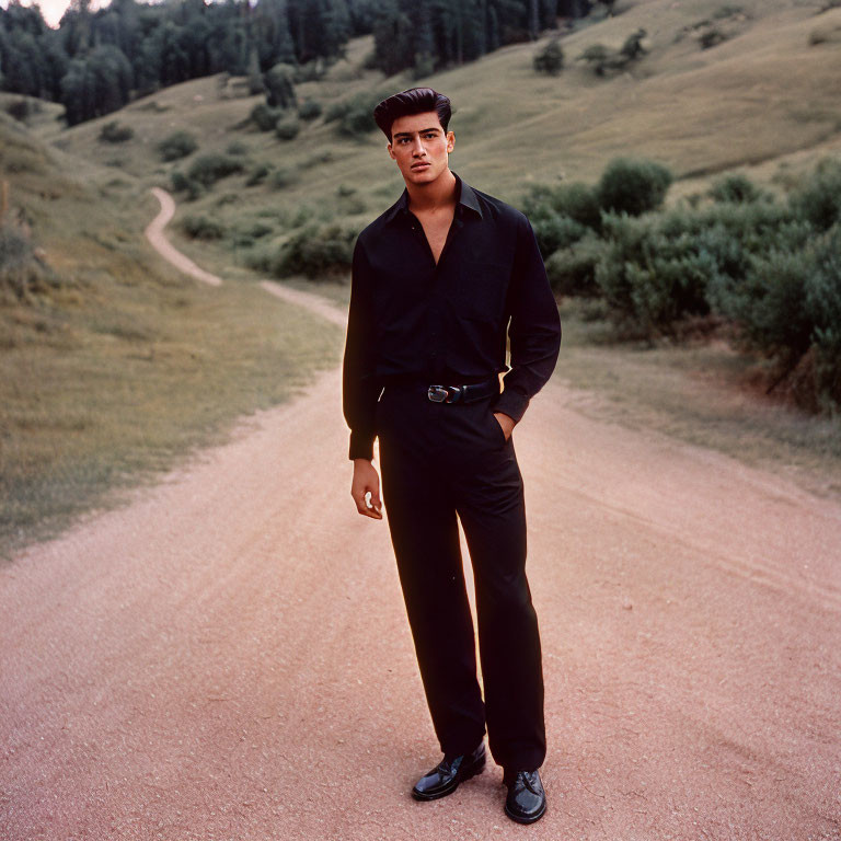 Man in Black Shirt Stands on Dirt Road with Grassy Hills