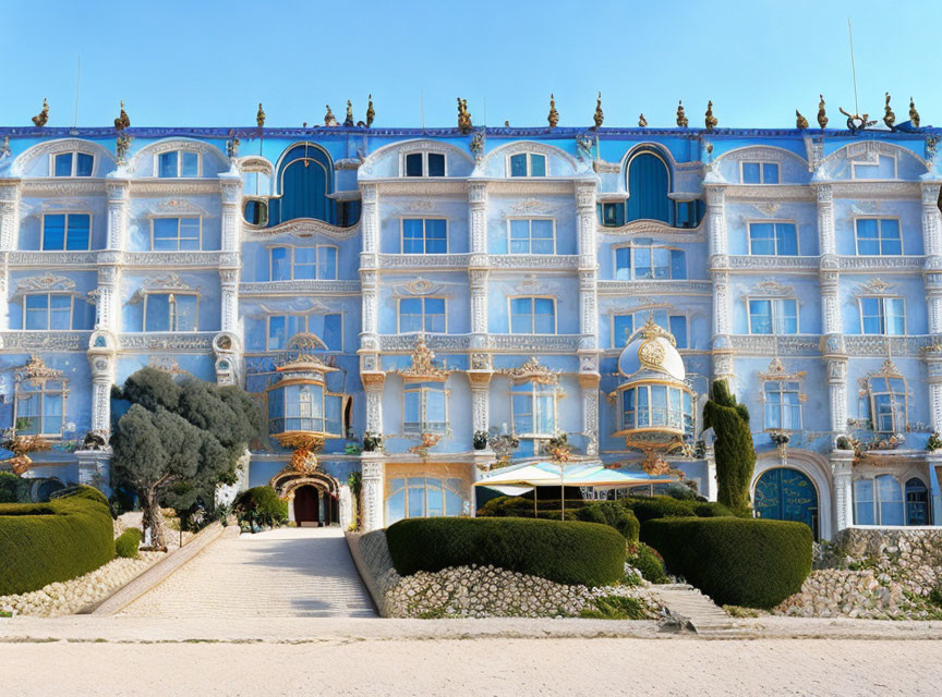 Ornate blue and white building with golden statues and manicured bushes