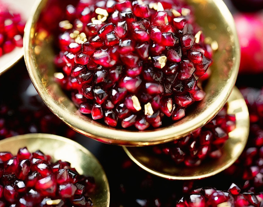 Colorful pomegranate seeds in golden bowl on dark surface