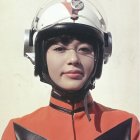 Freckled young woman in futuristic orange and white attire gazes ahead