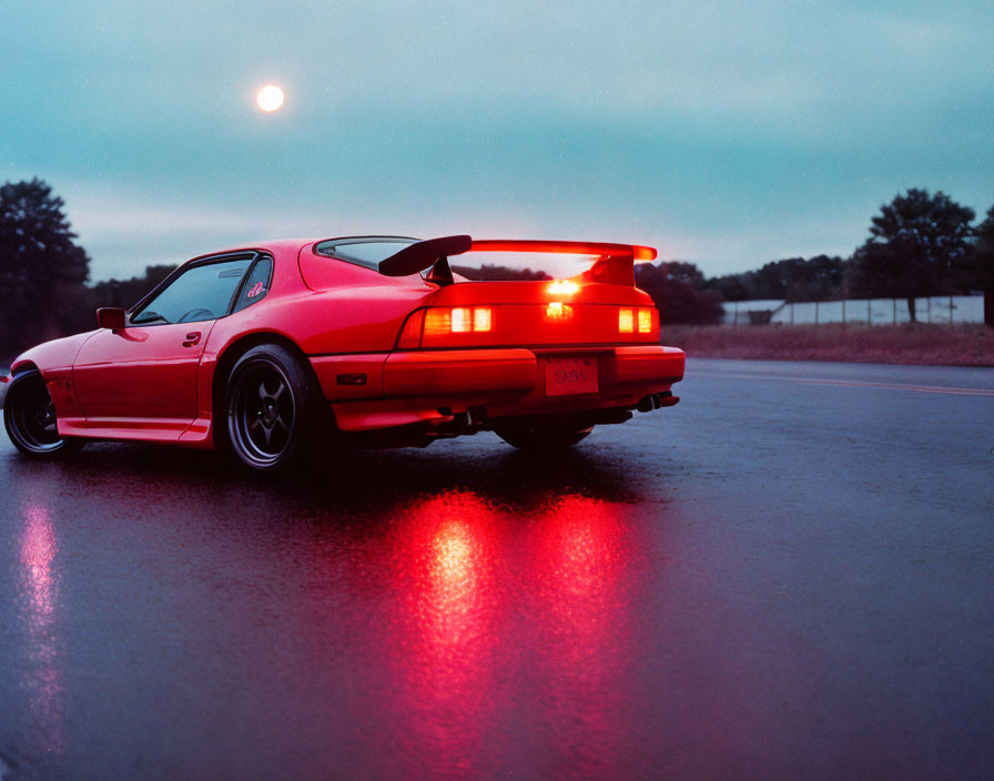 Red Sports Car with Brake Lights Parked on Wet Road at Twilight