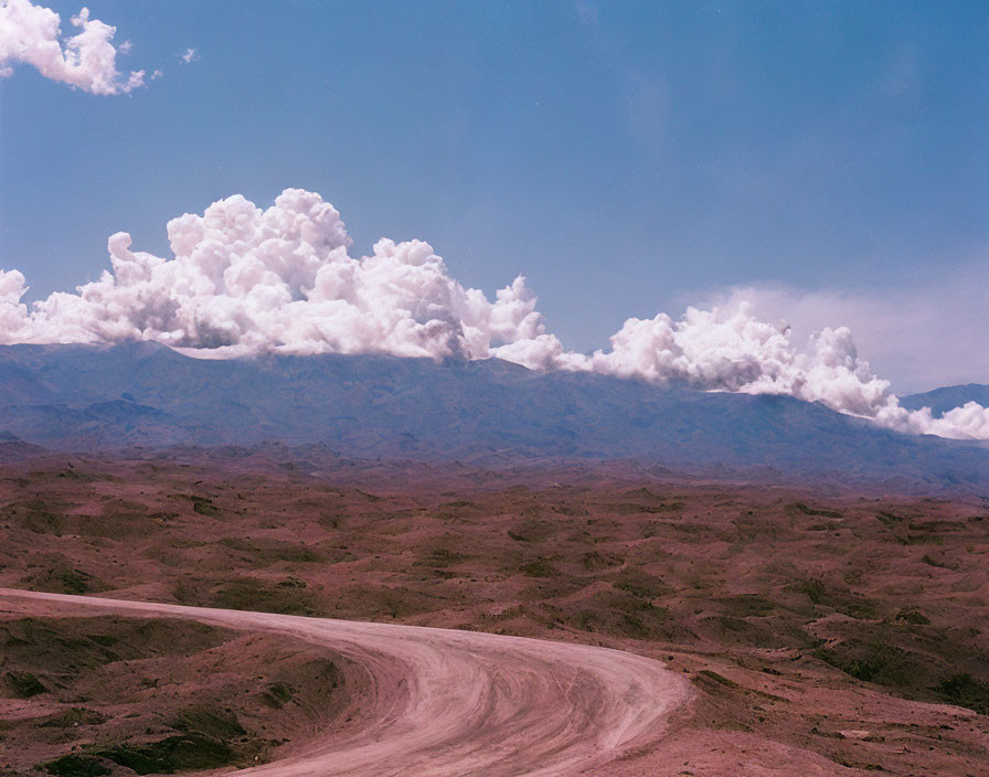 Barren landscape with winding dirt road and billowing clouds