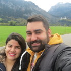 Gray-bearded man and dark-haired woman in front of scenic countryside.