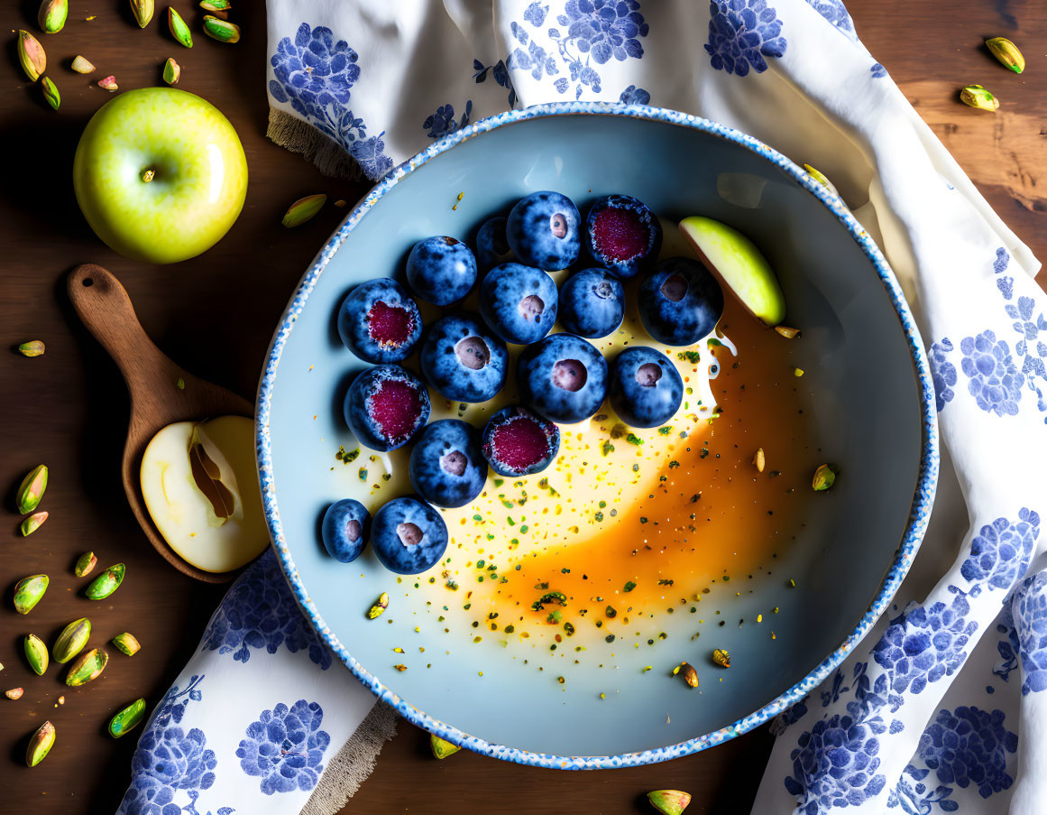 Yogurt bowl with blueberries, honey, pistachios, and sliced apples on wood surface