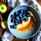 Yogurt bowl with blueberries, honey, pistachios, and sliced apples on wood surface