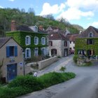 Tranquil rural landscape with stream, traditional houses, lush greenery, and cliffs