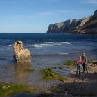 Person in straw hat admires beach view with lighthouse and cliff under clear sky