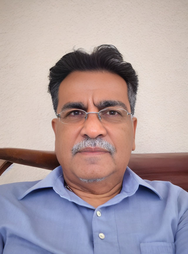 Middle-aged man with glasses and mustache in blue shirt against white wall