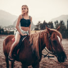 Woman in off-shoulder dress riding horse in scenic field with mountains.