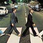 Men crossing zebra crossing on sunny street with parked cars and Volkswagen Beetle.