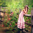 Woman in flowing dress leaning on wooden fence in blooming field at sunset