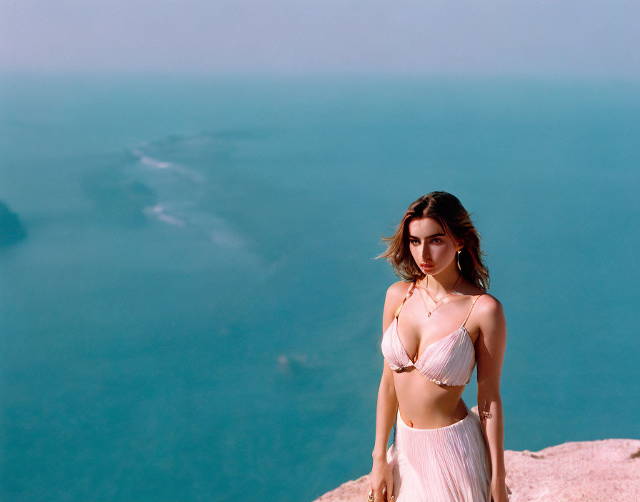 Person standing on cliff overlooking vast water under clear sky
