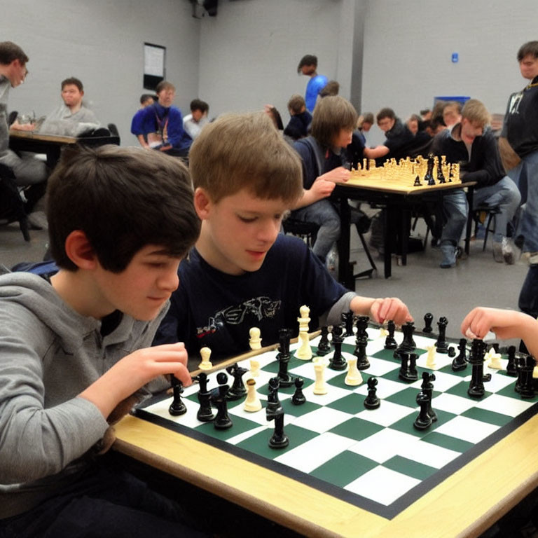 Young individuals playing chess in a well-lit room with others in the background