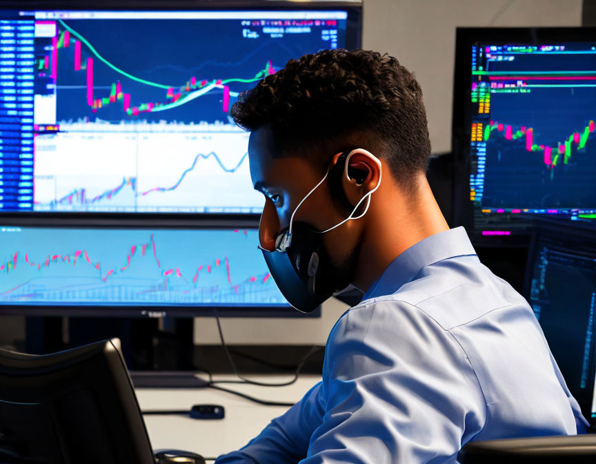 Man analyzing financial charts on multiple monitors in dimly lit office