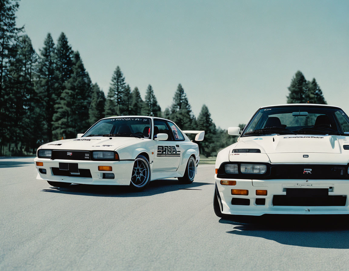 White Coupe and Hatchback Sports Cars Parked on Asphalt Road with Forest Background