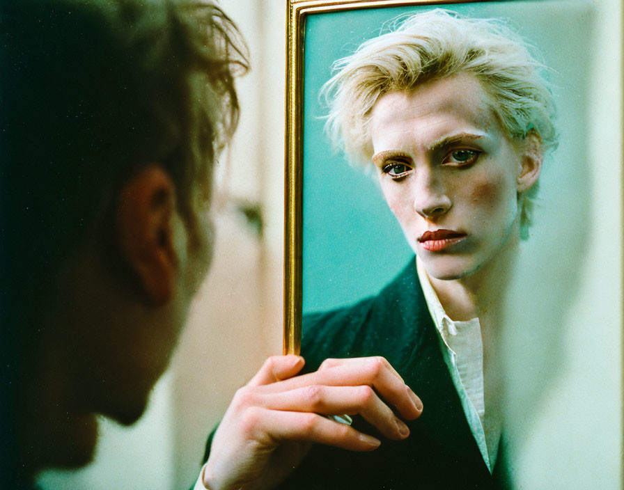 Blonde person with dark eye makeup gazes into mirror frame