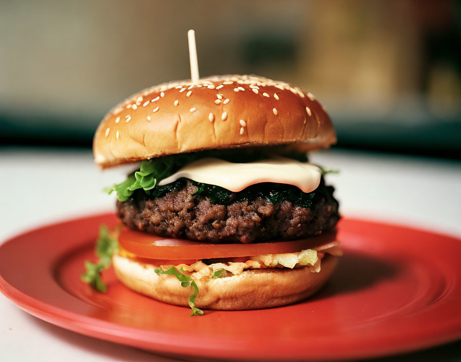 Classic Cheeseburger with Lettuce, Tomato, and Sauce on Sesame Seed Bun on Red Plate