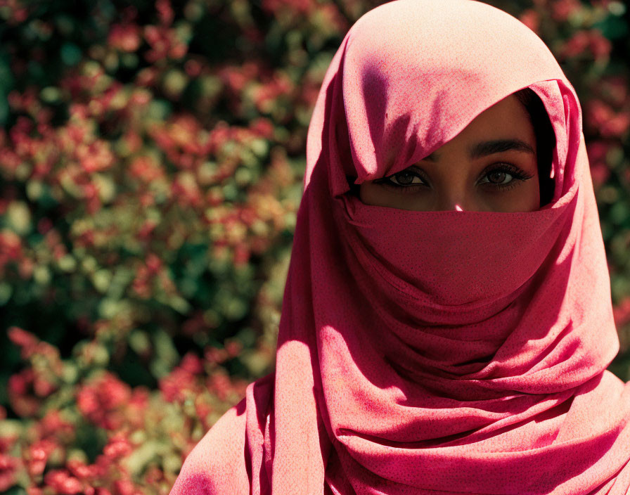 Woman in pink hijab with eyes visible amid red flowers