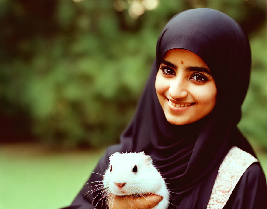 Smiling woman in hijab with white guinea pig on green background