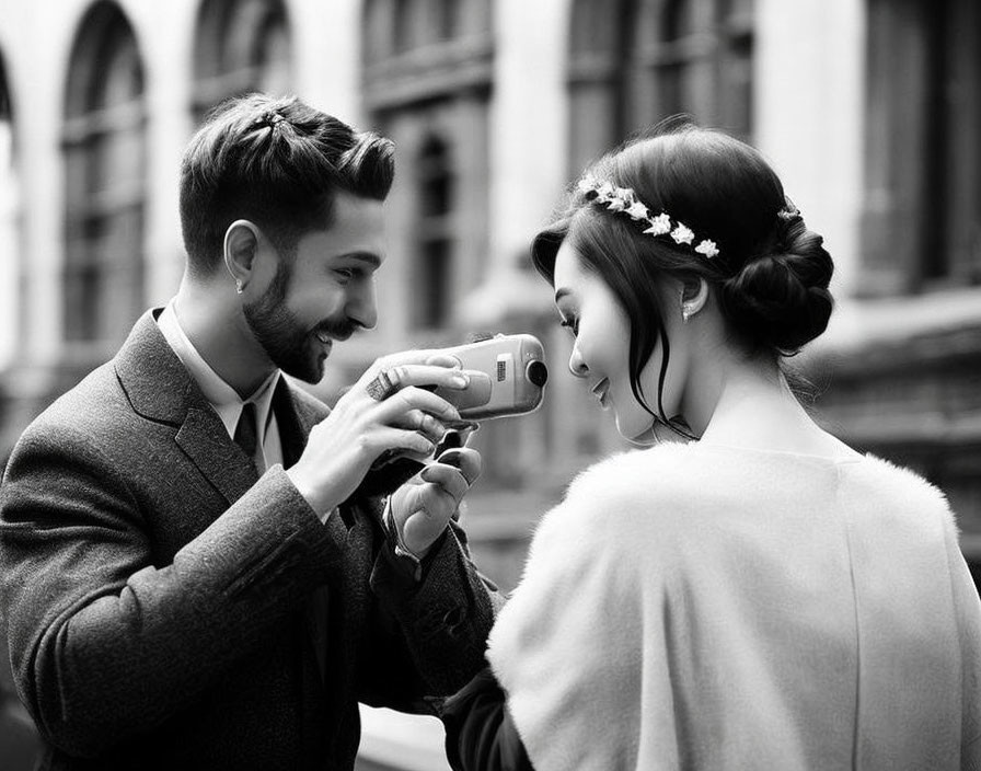 Monochrome image: Smiling man taking photo of woman with floral hair accessory