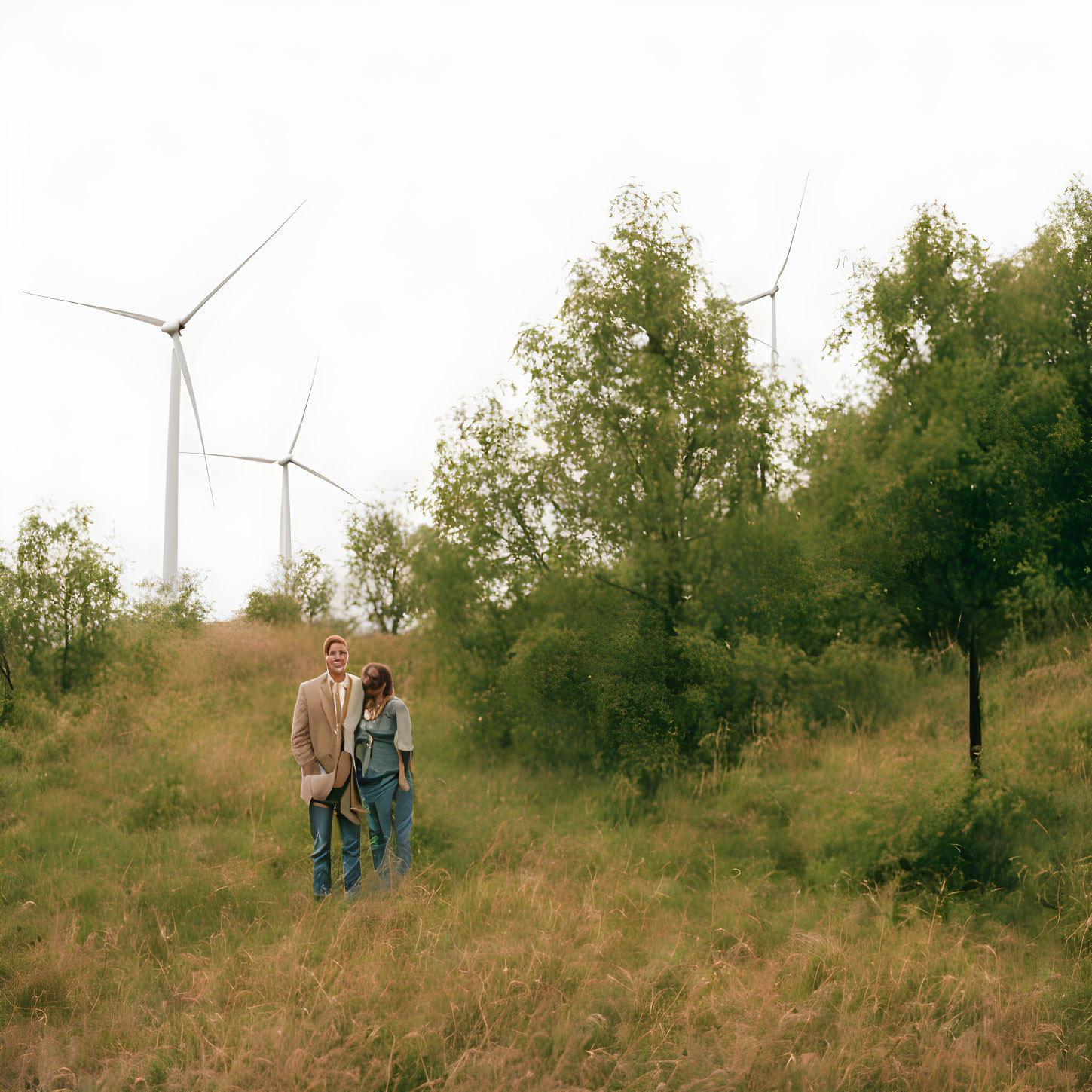 Couple in grassy field with wind turbines under overcast sky