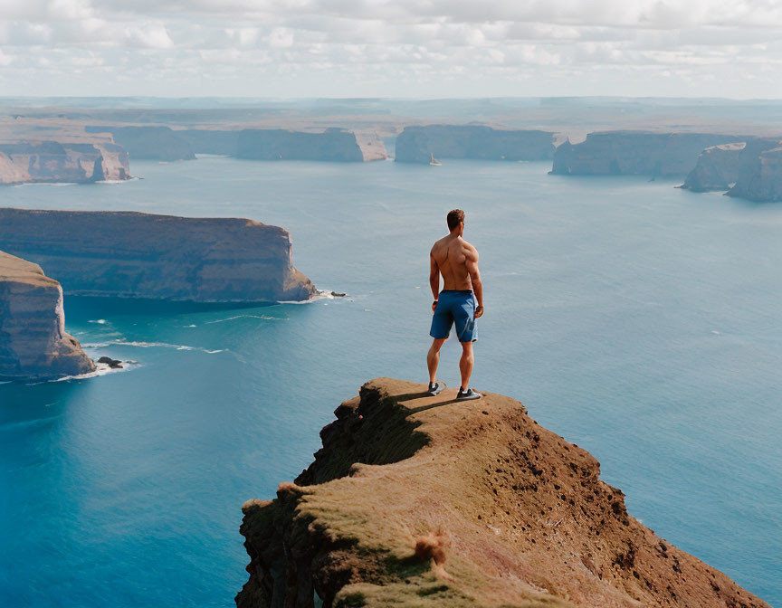 Shirtless man on cliff overlooking vast ocean