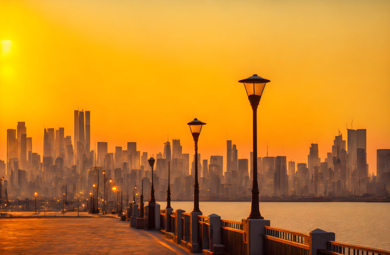 City skyline at sunset with orange glow and silhouetted skyscrapers viewed from waterfront promenade