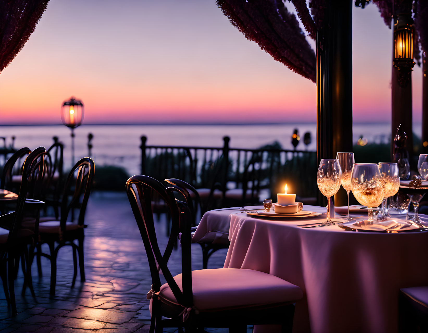 Romantic outdoor dining with candle, wine glasses, and ocean sunset view