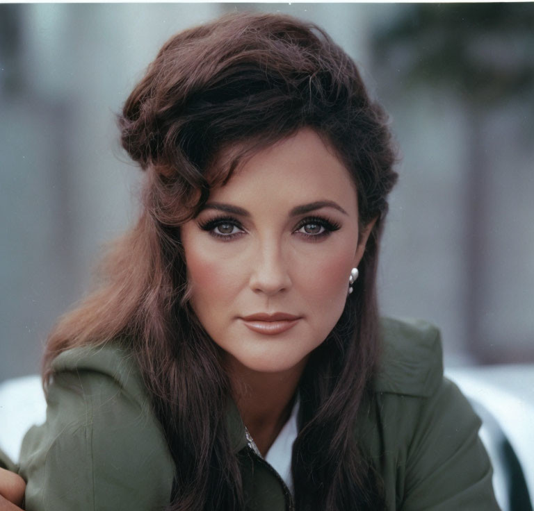 Brunet-haired woman in dramatic makeup and green outfit with pearl earrings.