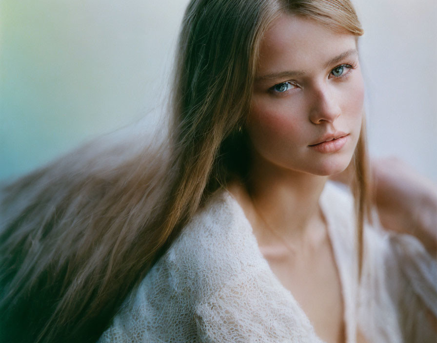 Young woman with light brown hair and blue eyes in off-white top gazes calmly.