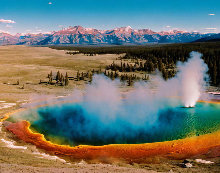 Colorful thermal pool surrounded by forest and mountains.