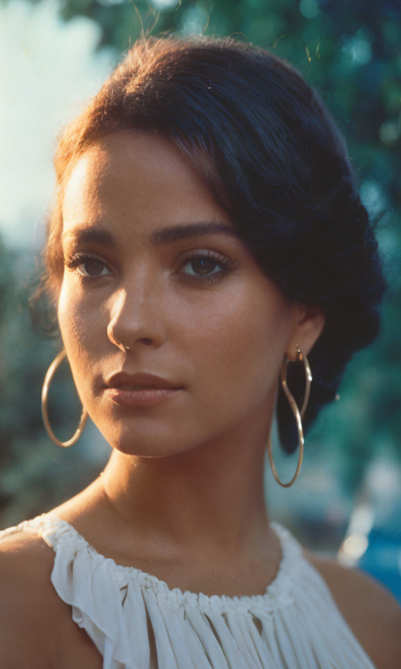 Dark-haired woman with hoop earrings in sunlight gaze away from camera.