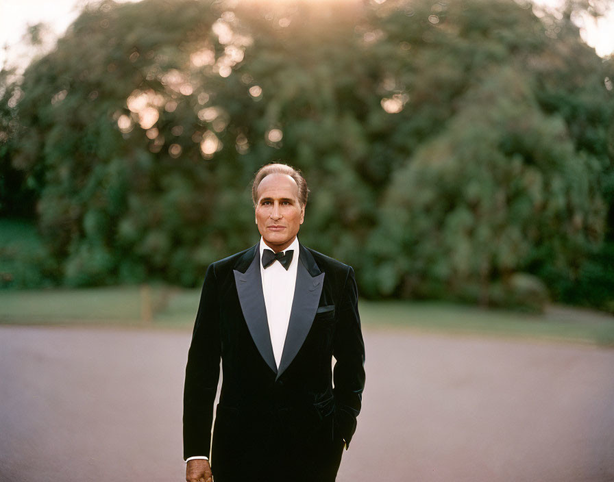 Formal person in tuxedo against sunset in lush green setting