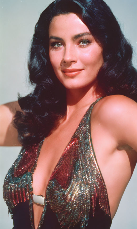 Dark-haired woman in low-cut, sparkling dress poses confidently.