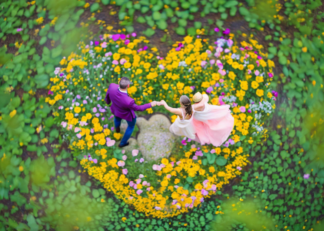 Couple spinning in heart-shaped flower arrangement in lush garden aerial view