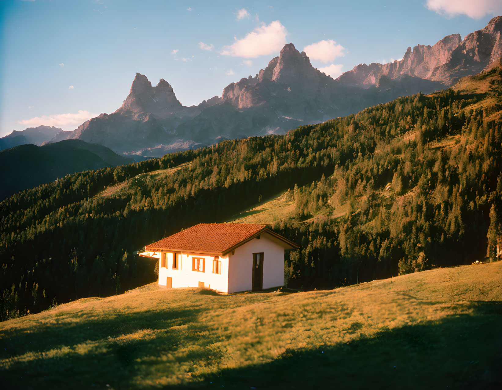 House on grassy hill with mountain backdrop at sunset